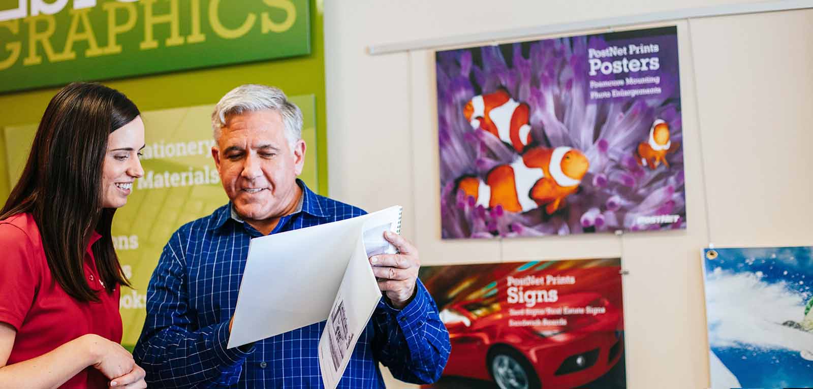 Postnet employee with design and print expertise helping customer with custom designed print materials.