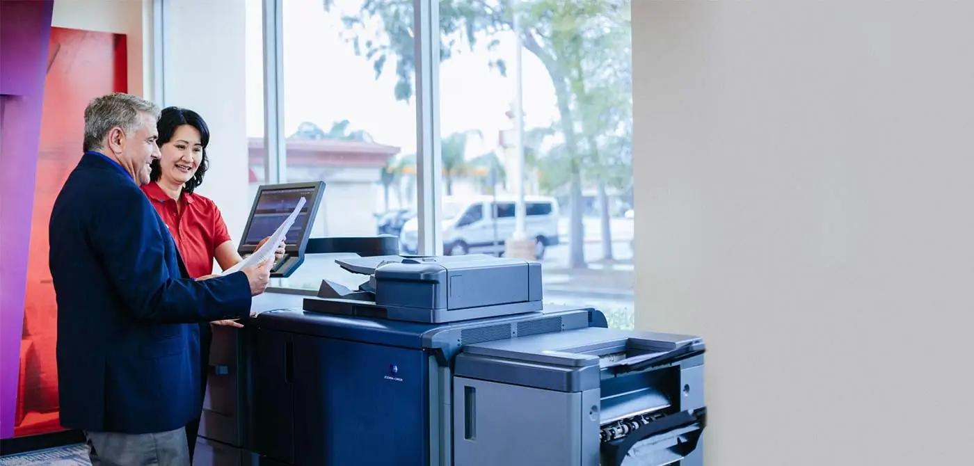 Photo of PostNet employee and customer reviewing documents next to a printer in a PostNet print shop.