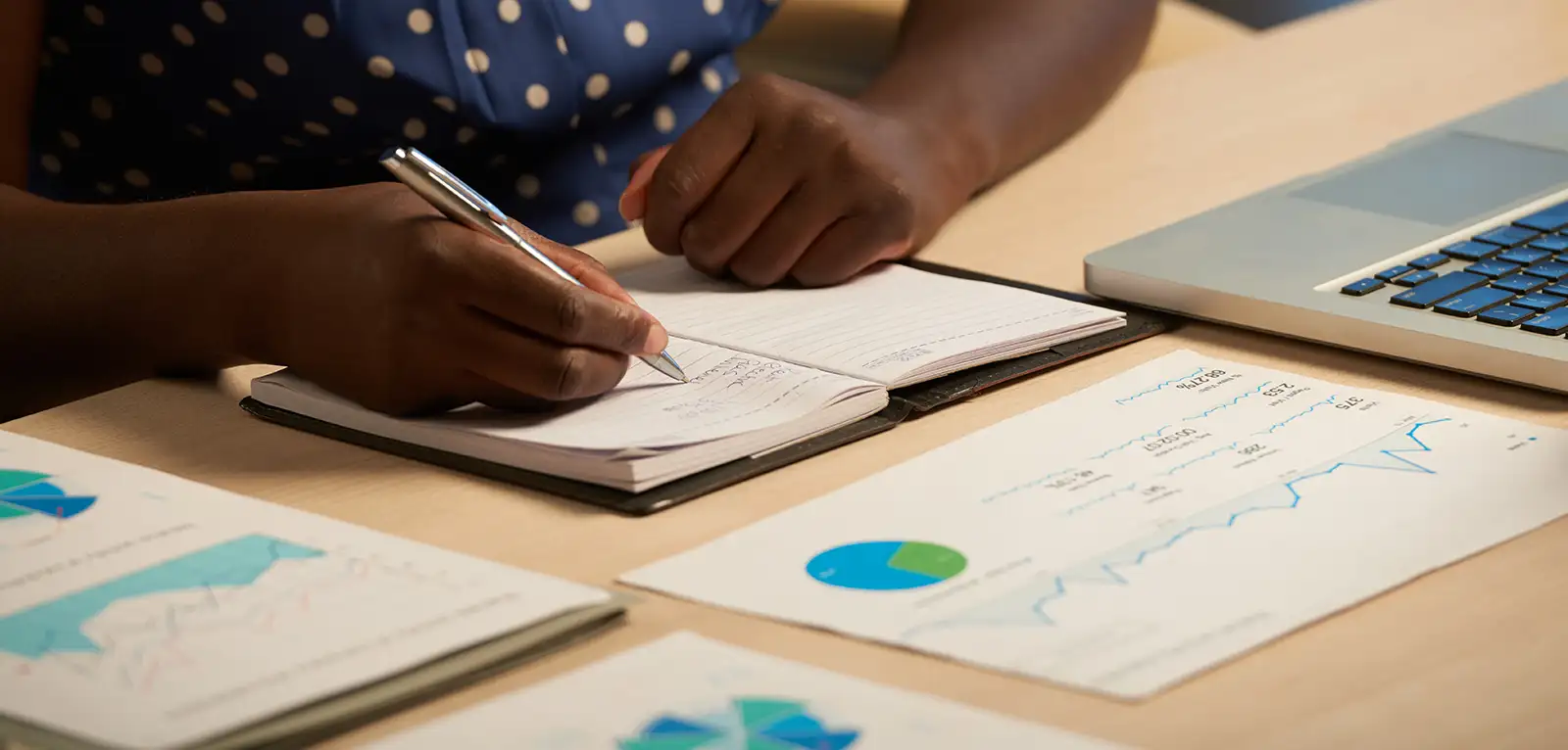 Someone at a desk writing in a notebook and looking at a chart