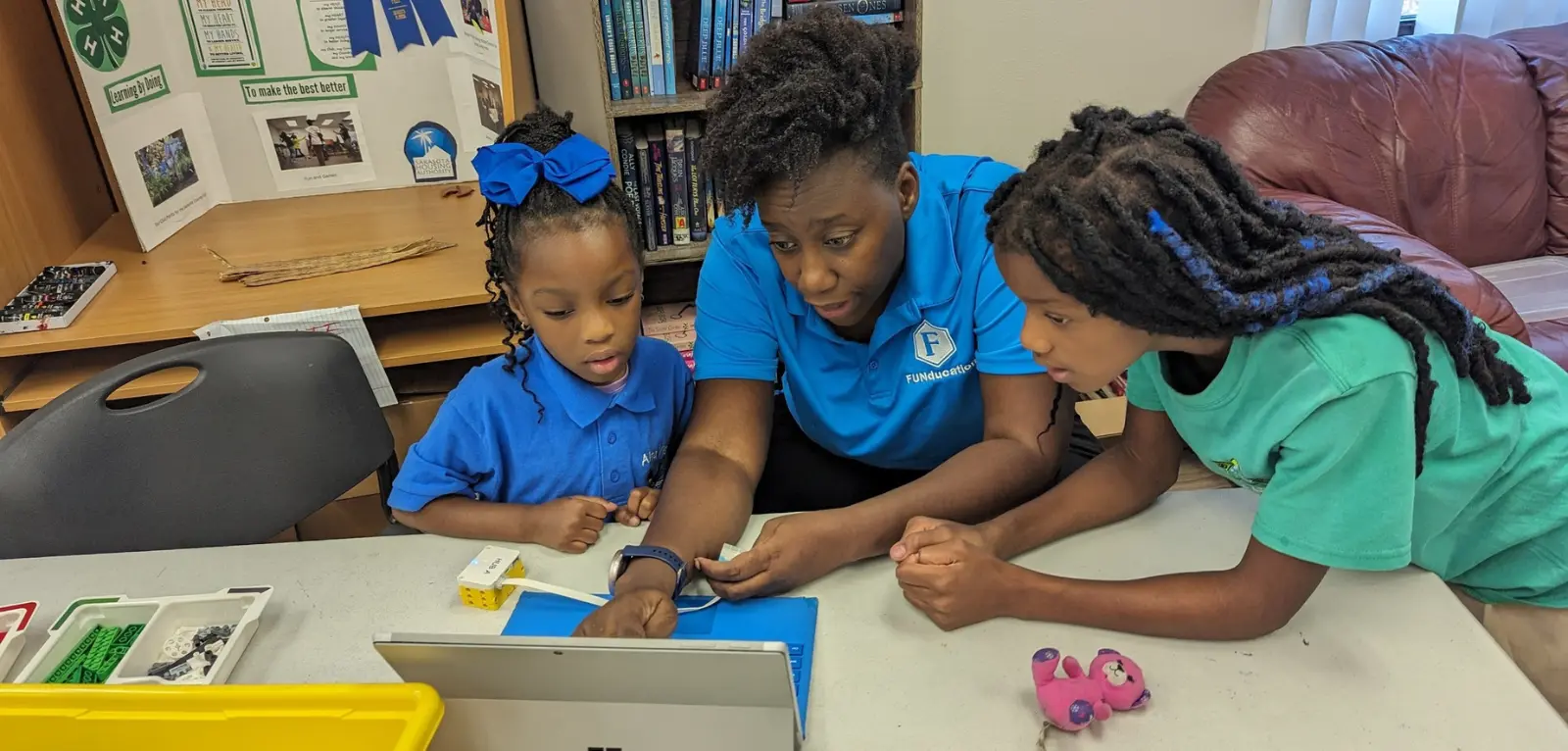 A woman helps two girls on a laptop